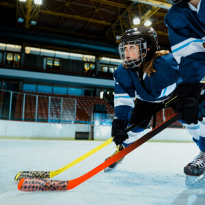 Boys playing ice hockey at indoors rink Cute boy learning to ice skate and play hockey with his couch at indoors rink. Staying next to goal and holding hockey stick